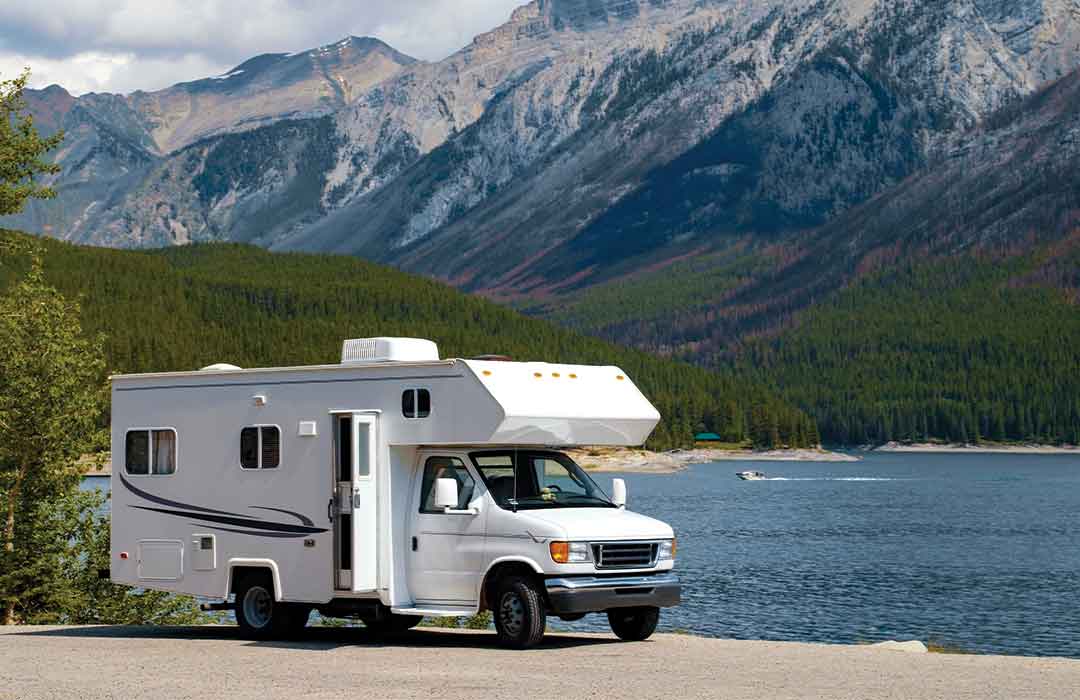 RV parked by lake with mountain backdrop.