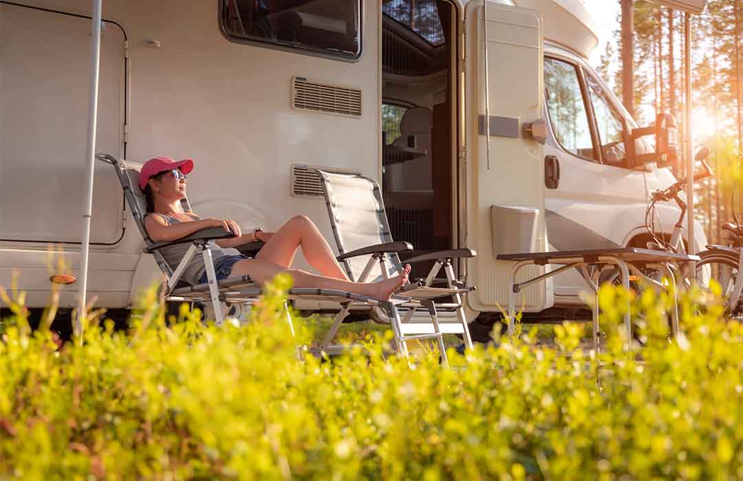 Person relaxing outside RV in sunny campsite.